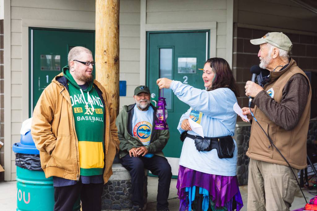 Sage Anderson presents the Purple Lantern to Joel Sunnhuber during the social held at the Deep Water Dock following the second annual 5K Run for Recovery on Saturday, Aug. 31, 2024, on the Homer Spit in Homer, Alaska. Also pictured are announcer Jamie Sutton (right) and Kachemak Bay Recovery Connection vice president Willy Dunne (rear center). Photo by Andrew Tomey