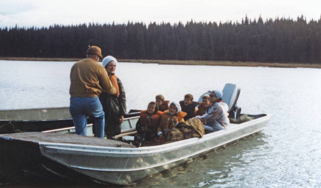 Jane Fair (standing, wearing white hat) receives help with her life jacket from Ron Hauswald prior to the Fair and Hauswald families embarking on an August 1970 cruise with Phil Ames on Tustumena Lake. Although conditions were favorable at first, the group soon encountered a storm that forced them ashore. (Photo courtesy of the Fair Family Collection)