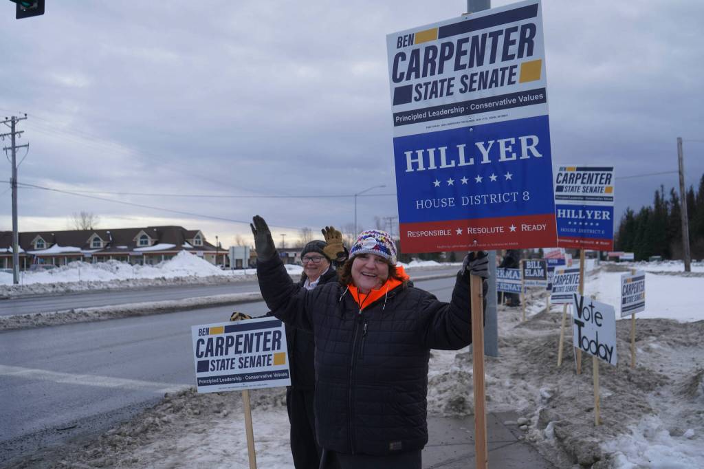 Cindy Roque waves signs for Ben Carpenter and John Hillyer along the Kenai Spur Highway in Kenai, Alaska, on Tuesday, Nov. 5, 2024. (Jake Dye/Peninsula Clarion)