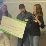 Homer Foundation Executive Director Stacey Schultz, left, receives from Jules and Dawn Ravin an honorary $1.2 million check to support youth in the community at the foundation's annual board meeting at the Kachemak Bay Campus in Homer, Alaska, Nov. 14, 2024. (Photo by Emilie Springer/Homer News)