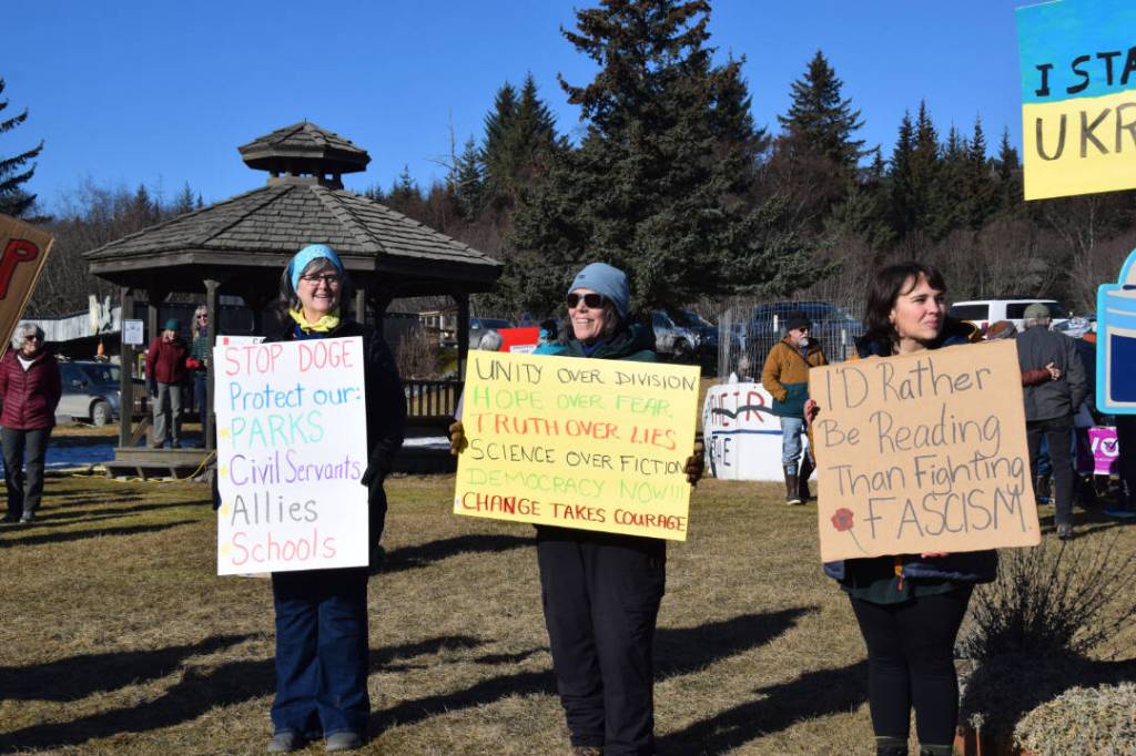 Community members hold up protest signs during the Stand for Democracy Rally on International Womens Day, March 8, 2025, at WKFL Park in Homer, Alaska. (Chloe Pleznac/Homer News)