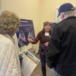 City of Homer Special Projects and Communications Coordinator Jenny Carroll points to a posterboard of one of the proposed harbor alternatives while talking with community members during the Homer Harbor Expansion public meeting on Saturday, March 15, 2025 at Kachemak Bay Campus. (Chloe Pleznac/Homer News)