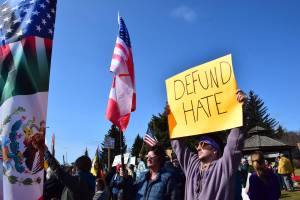 Protestors stand with an American flag and a sign that reads DEFUND HATE on Saturday, April 19 at WKFL Park during the Sustained Resistence, Makes a Difference Rally. (Chloe Pleznac/Homer News)