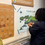 Aleyna Harris places magnets on the poster Olivia Holdaway created on Thursday, May 1, 2025, at Kachemak Bay Campus, in Homer, Alaska. (Chloe Pleznac/Homer News)