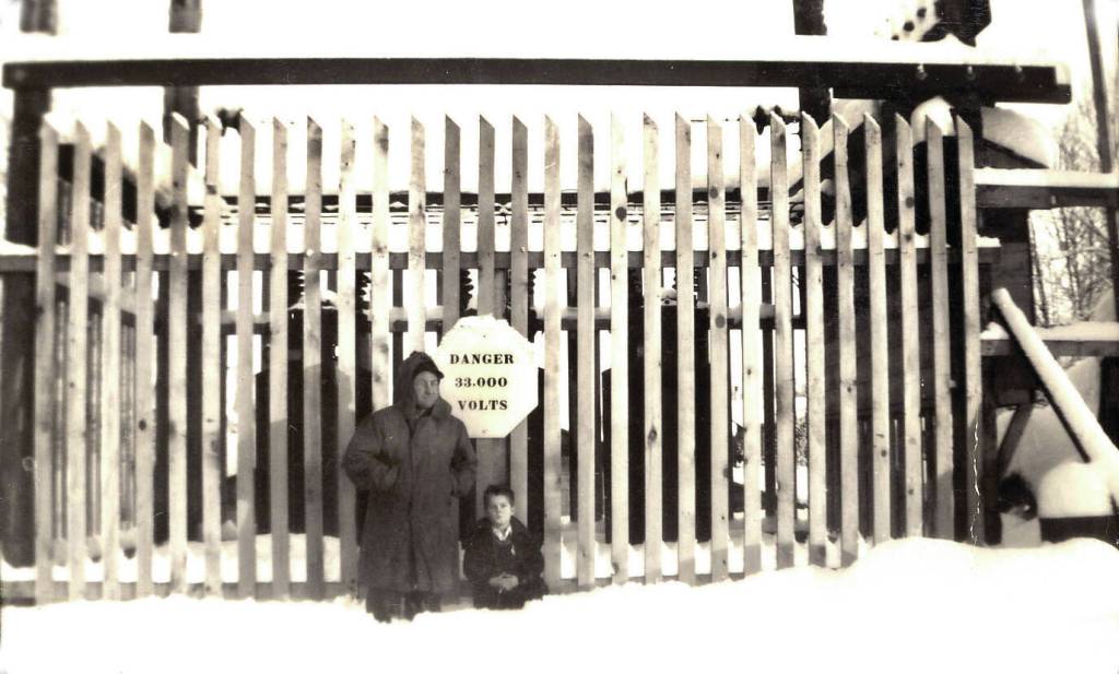 Photo courtesy of the Rowley Family
Frank Rowley and his youngest child, Raymond, stand in knee-deep snow in front of the protective fence around the main substation for Mountain View Light & Power in Anchorage in 1948 or 49. This photo was taken a year or two before Rowley moved to Kenai to begin supplying electrical power to the central peninsula.