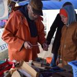 A volunteer from the Kachemak Bay Wooden Boat Society shows a young person how to measure out the wooden blocks needed to construct the perfect, toy wooden boat at the inaugural HomerFest on the Homer Spit on Saturday. (Chloe Pleznac/Homer News)