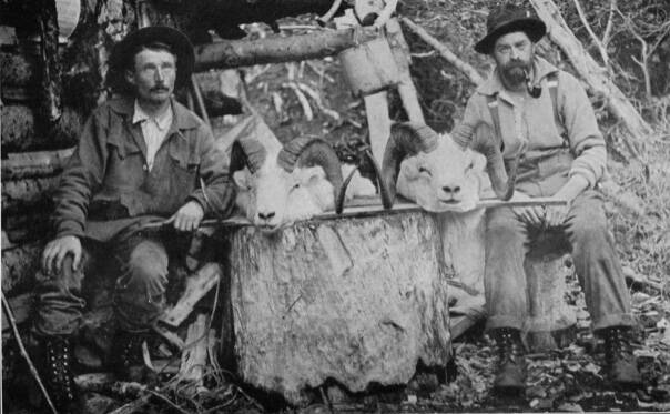 Photo from E. Marshall Sculls 1914 hunting memoir, Hunting in the Arctic and Alaska
Posing in front of Steve Melchiors cabin on the Killey River in 1912 are (left) packer/cook Ferdinand Fritz Posth and hunting guide William Wild Bill Dewitt, with two trophy Dall sheep heads.
