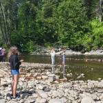 Community members watch ducks float by on the Anchor River during the annual Anchor River Duck Races on Saturday, July 5, 2025, in Anchor Point, Alaska. (Delcenia Cosman/Homer News)