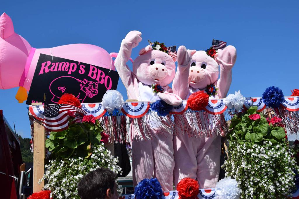 Two costumed pigs wave to the crowds on Pioneer Avenue from the Rumps BBQ float during the Fourth of July parade on Friday, July 4, 2025, in Homer, Alaska. (Delcenia Cosman/Homer News)