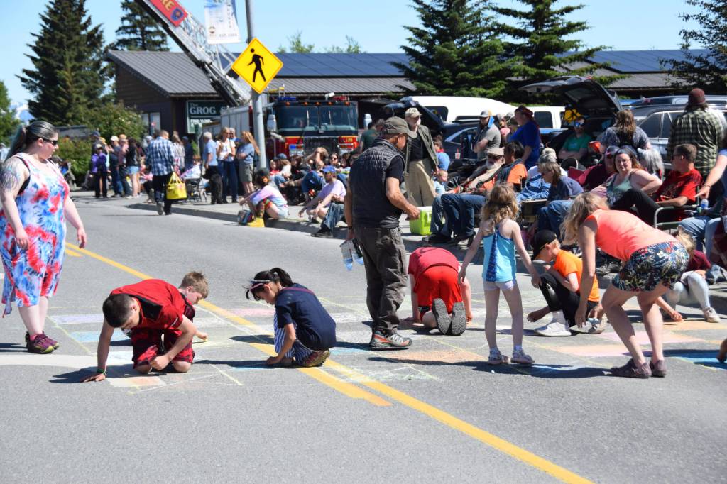 Kids color in a chalk chessboard on Pioneer Avenue in front of the Bay Realty judging station just before the start of the Fourth of July parade on Friday, July 4, 2025, in Homer, Alaska. (Delcenia Cosman/Homer News)