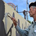 Artist Tom Reed begins to paint the silhouette of musician David Webster on July 2 in Homer, Alaska. Reed added 10 artists to the wall over the last few weeks, marking the end of the art project he began in 1985. (Chloe Pleznac/Homer News)