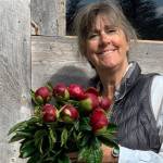Peony farmer and artist Gerri Martin hold a bouquet of budding Red Charm peonies in front of her packhouse of Diamond Ridge Road near Homer, Alaska. Photo provided by Gerri Martin
