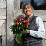 Peony farmer and artist Gerri Martin holds a bouquet of budding Red Charm peonies in front of her packhouse on Diamond Ridge Road near Homer, Alaska. Photo provided by Gerri Martin