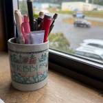 A vintage KBBI mug, repurposed and filled with various office supplies, rests in the Homer News office window on Friday, Aug. 8, 2025. (Chloe Pleznac/Homer News)