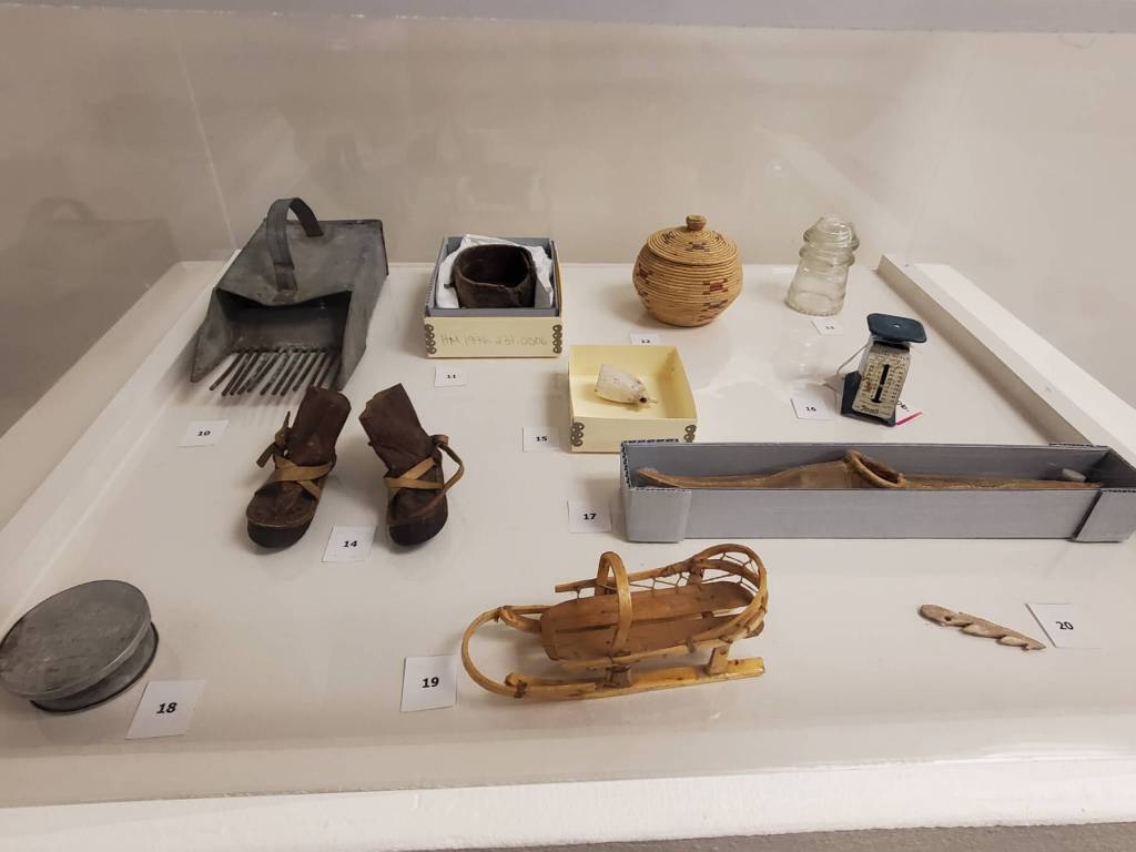 Items from the Pratt Museums permanent collection, including a berry scoop, wrapped bark and woven baskets, model mukluks, a postal letter scale, model dog sled, harpoon head and more, are displayed alongside the Homer High School Alaska History classs exhibit on Friday, Dec. 5, 2025, in the museums downstairs classroom in Homer, Alaska. (Delcenia Cosman/Homer News)