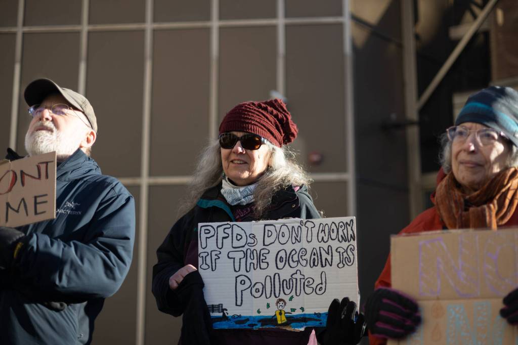 Larri Spengler holds a sign reading PFDs dont work if the ocean is polluted during an anti-LNG pipeline protest led by the Juneau-Douglas High School: Yadaa.at Kalé chapter of Alaska Youth for Environmental Action outside the Alaska State Capitol on Saturday, Jan. 24<ins>, 2026</ins>.