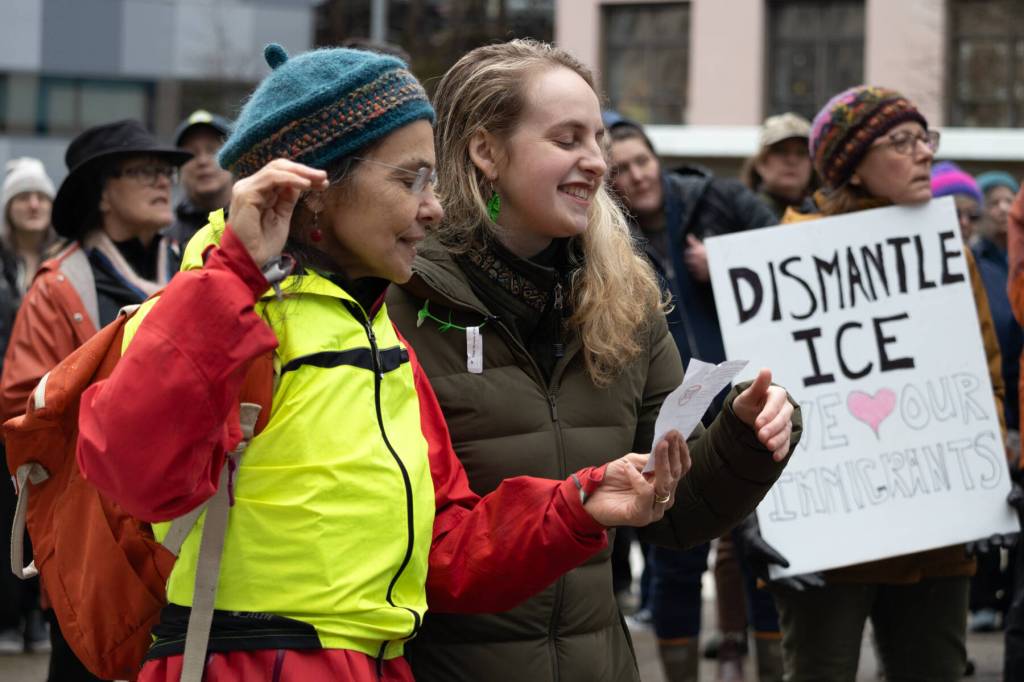 Event organizers Laura Stats, left, and Ariel Hasse-Zamudio sing lyrics off a page to an original song by Eric Antrim, a local musician and Forest Service employee. If we want to say, Dont forget Alex, now is the time, the crowd sang from pages with the lyrics. If we want to say we love our neighbors … now is the time.