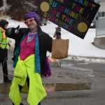 A community member walking with the Kachemak Bay Recovery Connection float holds up a sign that reads, If you cant find the sunshine, be the sunshine, during the Winter Carnival Parade on Saturday, Feb. 14, 2026, in Homer, Alaska. (Delcenia Cosman/Homer News)