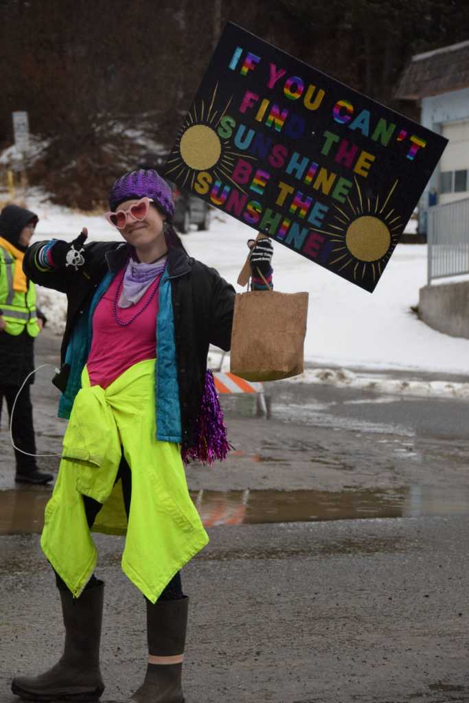 A community member walking with the Kachemak Bay Recovery Connection float holds up a sign that reads, If you cant find the sunshine, be the sunshine, during the Winter Carnival Parade on Saturday, Feb. 14, 2026, in Homer, Alaska. (Delcenia Cosman/Homer News)