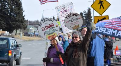 Protesters line up along Pioneer Avenue and hold up signs that read, No Crowns for Clowns and Trump for Prison, Make America Safe Again, during the third nationally-organized No Kings protest on Saturday, March 28, 2026, in Homer, Alaska. (Delcenia Cosman/Homer News)