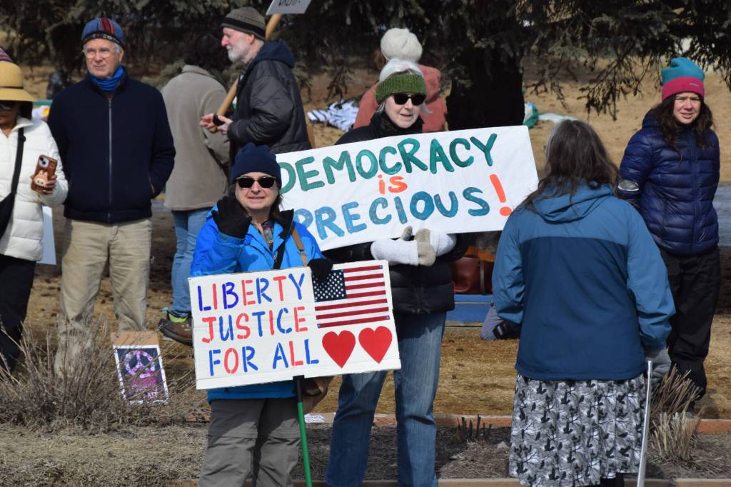 Community members hold up signs that read Liberty (and) justice for all and Democracy is Precious during the No Kings protest on Saturday, March 28, 2026, in Homer, Alaska. (Delcenia Cosman/Homer News)