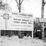 Photo from the Kenai Peninsula College photo archive
Signs of the times at Soldotnas Lutheran Church, which was still under construction in the early 1960s. The small sign on the birch tree reads, Temporarily Meeting at Soldatna Theater.
